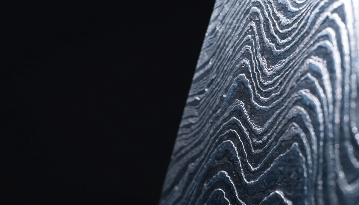 Macro d'une lame en damas forgé, les couches d'acier révélées par une lumière rasante